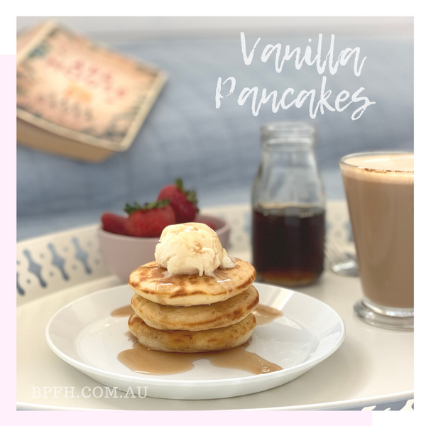 Vanilla pancake stack with vanilla ice cream and maple syrup, on a breakfast tray with coffee and fresh strawberries